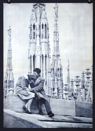 a man and woman sitting on a ledge kissing