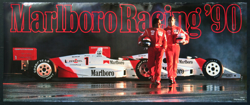 two men in red racing suits walking next to a race car